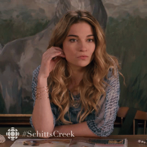 A Woman Is Sitting At A Table With A #Schittscreek Logo On The Bottom GIF