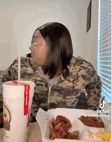 A Woman Is Sitting At A Table With A Tray Of Food And A Drink . GIF