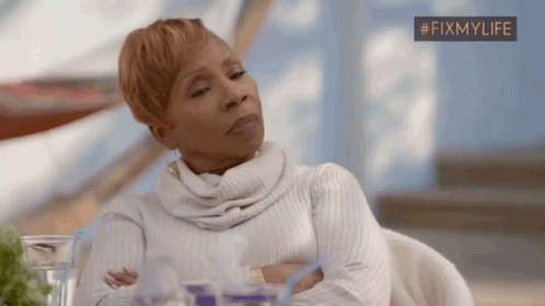 A Woman Is Sitting At A Table With Her Arms Crossed And Looking At Something . GIF