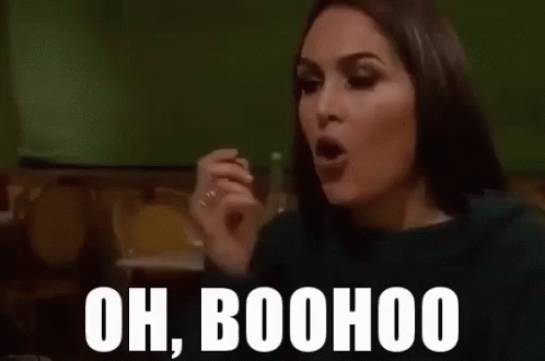 A Woman Is Sitting At A Table With Her Hand Up And The Words `` Oh Boohoo '' Written On Her Face . GIF
