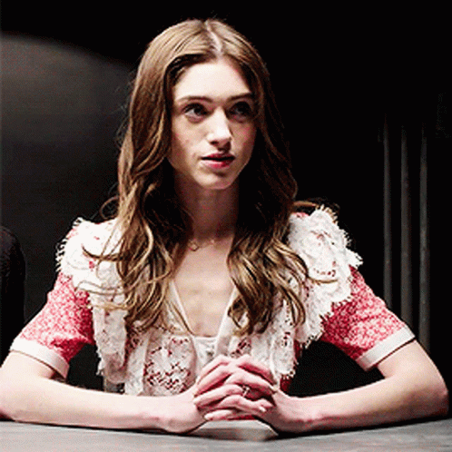 A Woman Is Sitting At A Table With Her Hands Folded In Front Of Her GIF