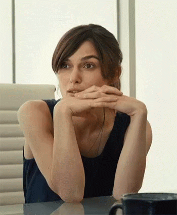 A Woman Is Sitting At A Table With Her Hands On Her Chin GIF