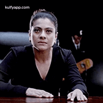 A Woman Is Sitting At A Table With Her Hands On The Table And Making A Funny Face . GIF