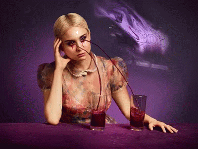 a woman is sitting at a table with two glasses of red liquid being poured into her