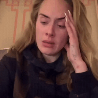 A Woman Is Sitting Down With Her Hand On Her Forehead And Making A Funny Face . GIF