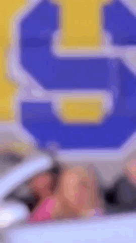A Woman Is Sitting In A Car In Front Of A Blue And Yellow Sign That Says S. GIF