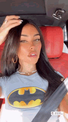 A Woman Is Sitting In A Car Wearing A Batman T-Shirt And Earrings . GIF