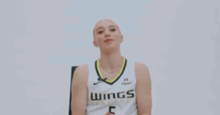 A Woman Is Sitting In A Chair And Smiling While Wearing A Basketball Uniform . GIF