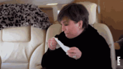 A Woman Is Sitting In A Chair Eating A Piece Of Food . GIF