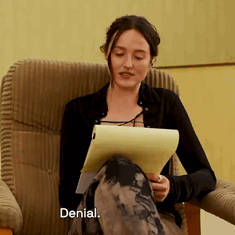 A Woman Is Sitting In A Chair Holding A Piece Of Paper And The Word Denial Is Next To Her GIF
