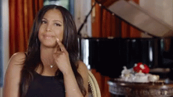 A Woman Is Sitting In A Chair In Front Of A Piano And Pointing To Her Face . GIF