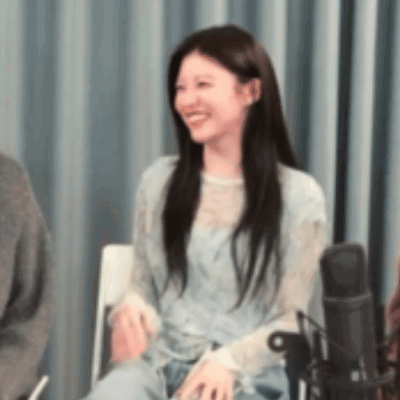 A Woman Is Sitting In A Chair Smiling In Front Of A Microphone In A Room . GIF