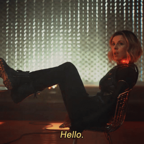 A Woman Is Sitting In A Chair With Her Feet Up And The Words Hello Behind Her GIF
