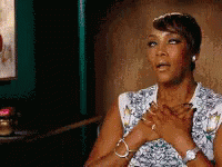 A Woman Is Sitting In A Chair With Her Hands On Her Heart . GIF