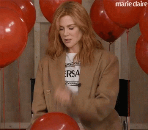 A Woman Is Sitting In A Chair With Red Balloons And Confetti Falling On Her . GIF