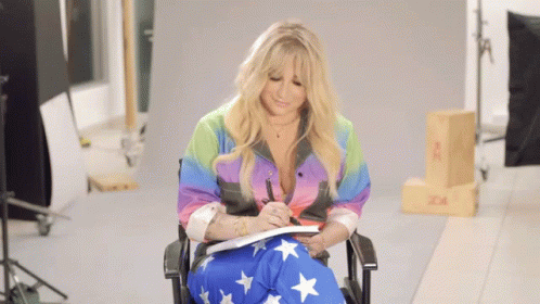 A Woman Is Sitting In A Chair Writing In A Notebook GIF