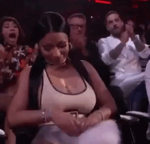 A Woman Is Sitting In A Crowd Of People And Holding A Cell Phone . GIF