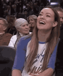 A Woman Is Sitting In A Crowd Of People Laughing . GIF