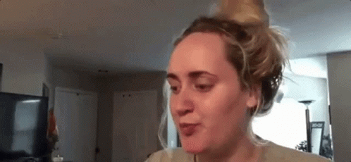 A Woman Is Sitting In A Living Room With Her Hair In A Bun And Making A Funny Face . GIF