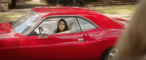 A Woman Is Sitting In A Red Car With Her Head Out The Window . GIF