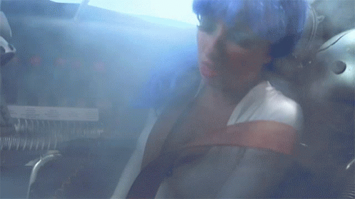 A Woman Is Sitting In A Room With A Smoke Coming Out Of Her Mouth GIF