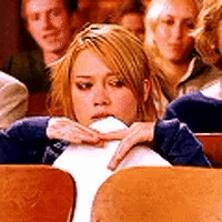 A Woman Is Sitting In A Row Of Wooden Chairs With Her Hand On Her Face . GIF