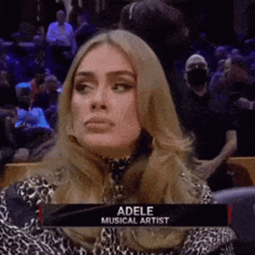 A Woman Is Sitting In A Stadium With A Sign That Says Adele Musical Artist On It . GIF