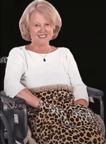 A Woman Is Sitting In A Wheelchair With A Leopard Print Blanket On Her Lap . GIF