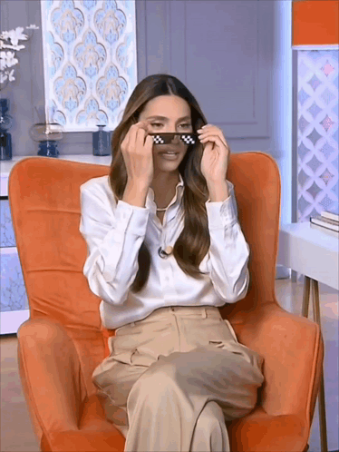 A Woman Is Sitting In An Orange Chair And Wearing Sunglasses GIF