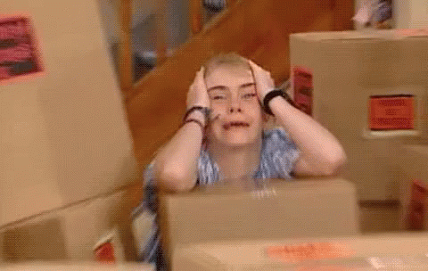 A Woman Is Sitting In Front Of A Box With Her Hands On Her Head And Making A Funny Face . GIF