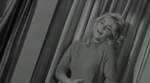 A Woman Is Sitting In Front Of A Curtain In A Black And White Photo GIF