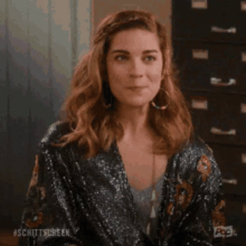 A Woman Is Sitting In Front Of A Filing Cabinet And Smiling While Holding Her Hair . GIF