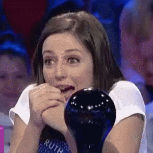A Woman Is Sitting In Front Of A Glass Ball With Her Mouth Open And Looking At It . GIF