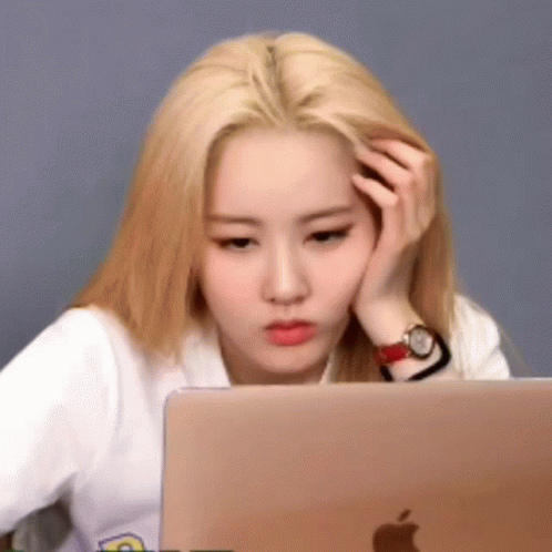 A Woman Is Sitting In Front Of A Laptop Computer With Her Hand On Her Forehead . GIF