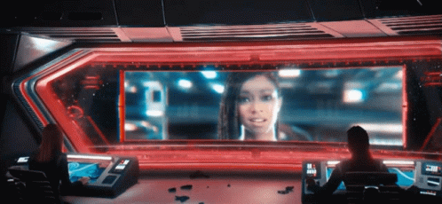 A Woman Is Sitting In Front Of A Large Screen That Says ' A ' On It GIF
