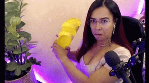 A Woman Is Sitting In Front Of A Microphone Holding A Yellow Object . GIF