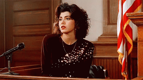 A Woman Is Sitting In Front Of A Microphone In A Courtroom GIF