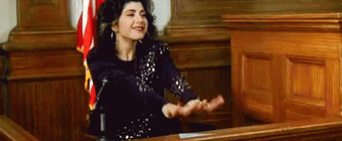 A Woman Is Sitting In Front Of A Microphone In A Courtroom With Her Hands Outstretched . GIF