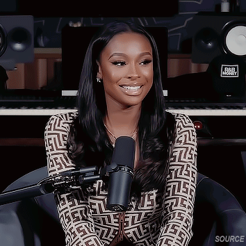 A Woman Is Sitting In Front Of A Microphone In A Recording Studio And Smiling . GIF