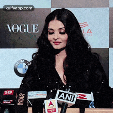 A Woman Is Sitting In Front Of A Microphone In Front Of A Sign That Says Vogue . GIF