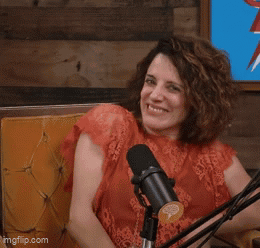 A Woman Is Sitting In Front Of A Microphone With Her Eyes Closed And Her Hands In The Air GIF