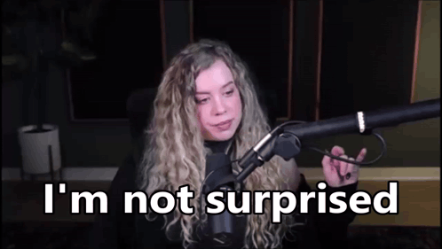 A Woman Is Sitting In Front Of A Microphone With The Words `` I 'M Not Surprised '' Written On The Screen . GIF