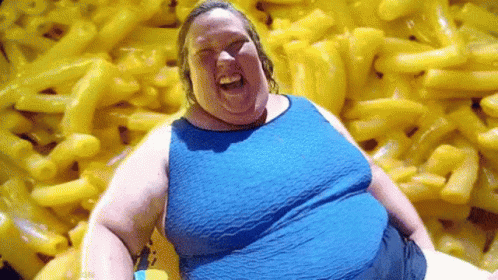 A Woman Is Sitting In Front Of A Pile Of Macaroni And Cheese . GIF
