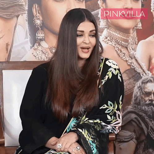 A Woman Is Sitting In Front Of A Pinkvilla Poster GIF