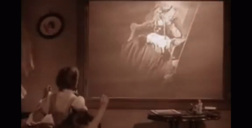 A Woman Is Sitting In Front Of A Projector Screen With A Picture On It GIF