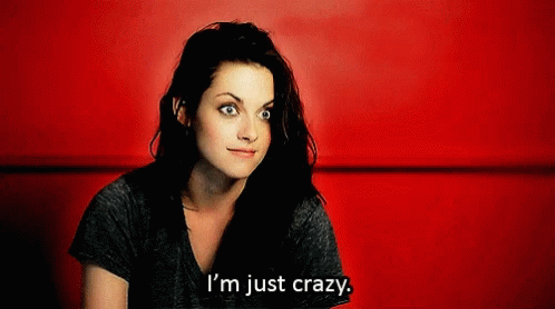 A Woman Is Sitting In Front Of A Red Wall And Says " I 'M Just Crazy " GIF