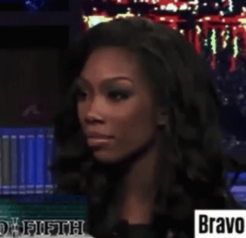 A Woman Is Sitting In Front Of A Sign That Says Bravo On It . GIF
