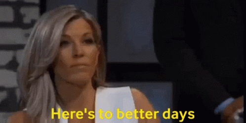 A Woman Is Sitting In Front Of A Sign That Says Here 'S To Better Days GIF