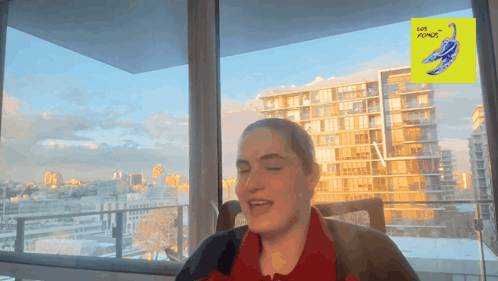 A Woman Is Sitting In Front Of A Window With A Yellow Sign That Says Love Plumes On It GIF