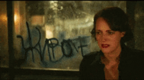 a woman is sitting in front of a window with graffiti on it that says ' riot '